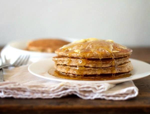 Whole wheat pancakes stacked on a plate with syrup.