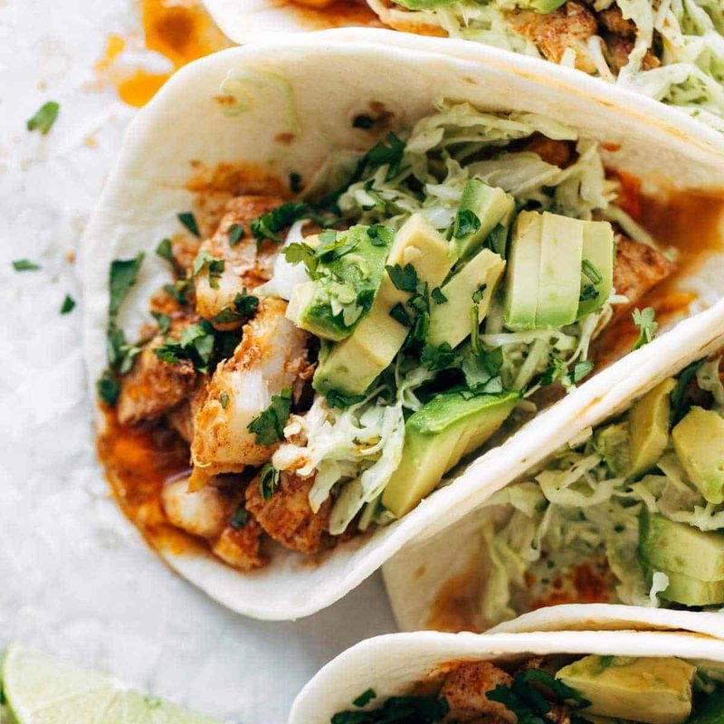 Fish tacos with avocados and a wedge of lime next to them.