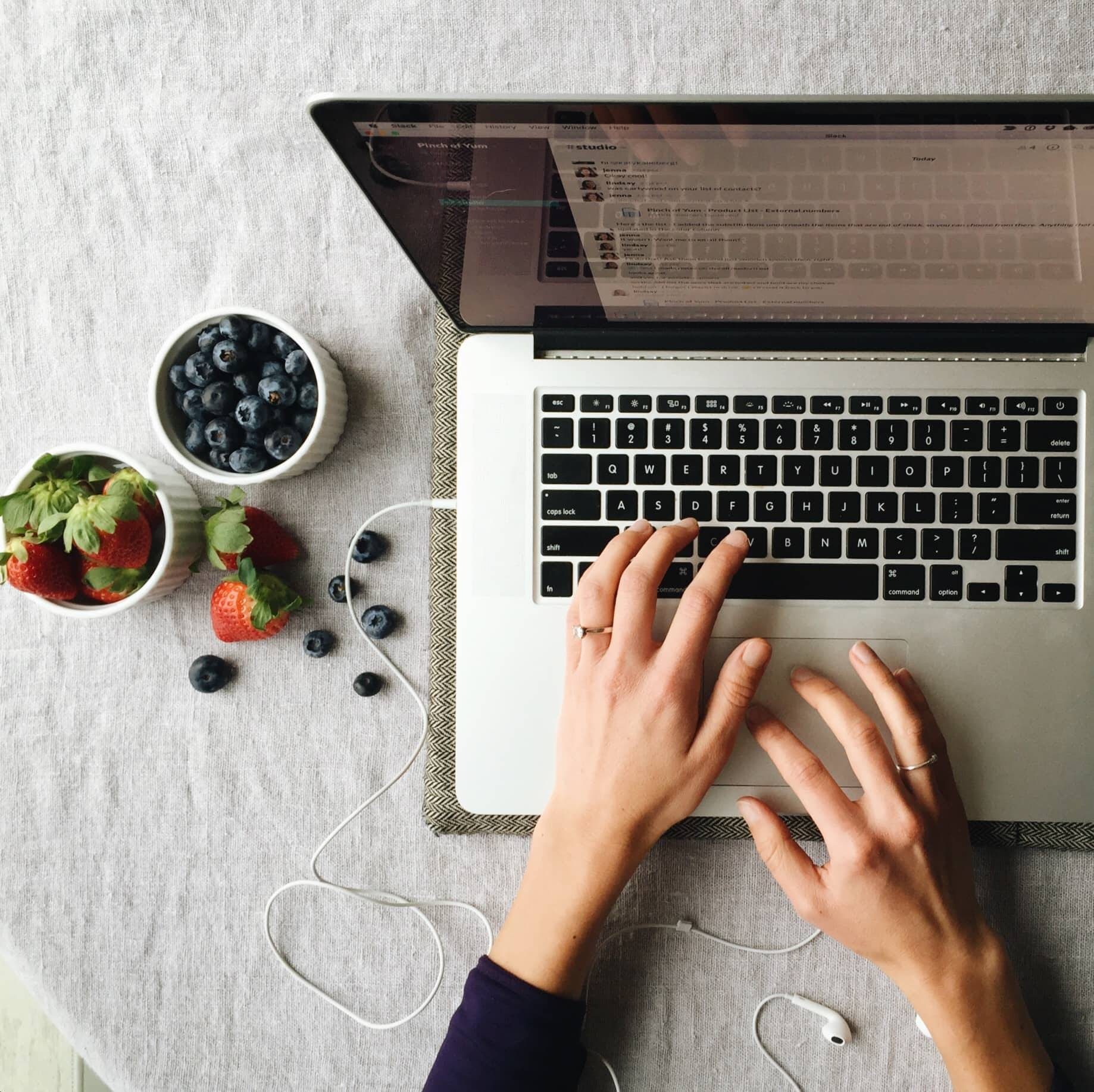 hands on a laptop keyboard with strawberries and blueberries