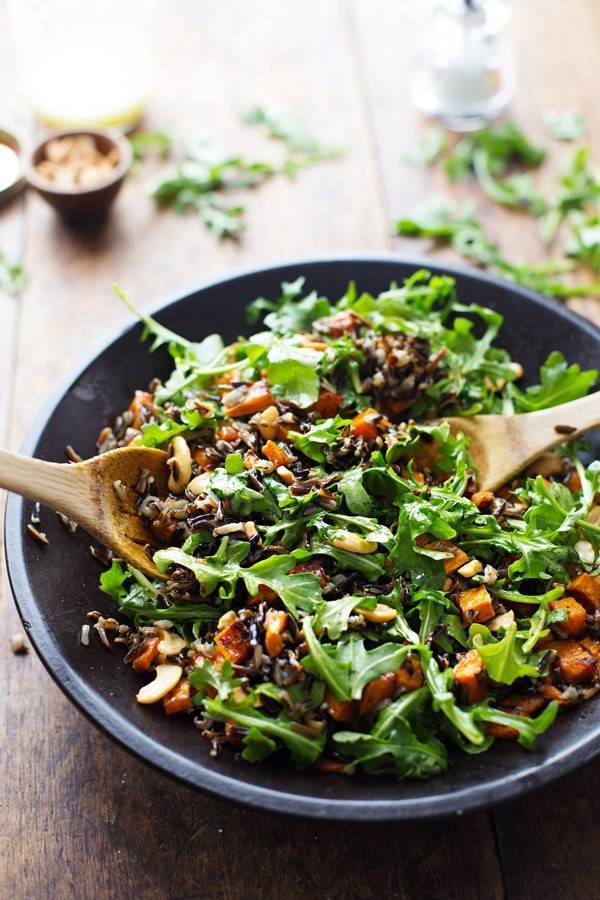 Roasted Sweet Potato, Wild Rice, and Arugula Salad in a bowl with wooden spoons.