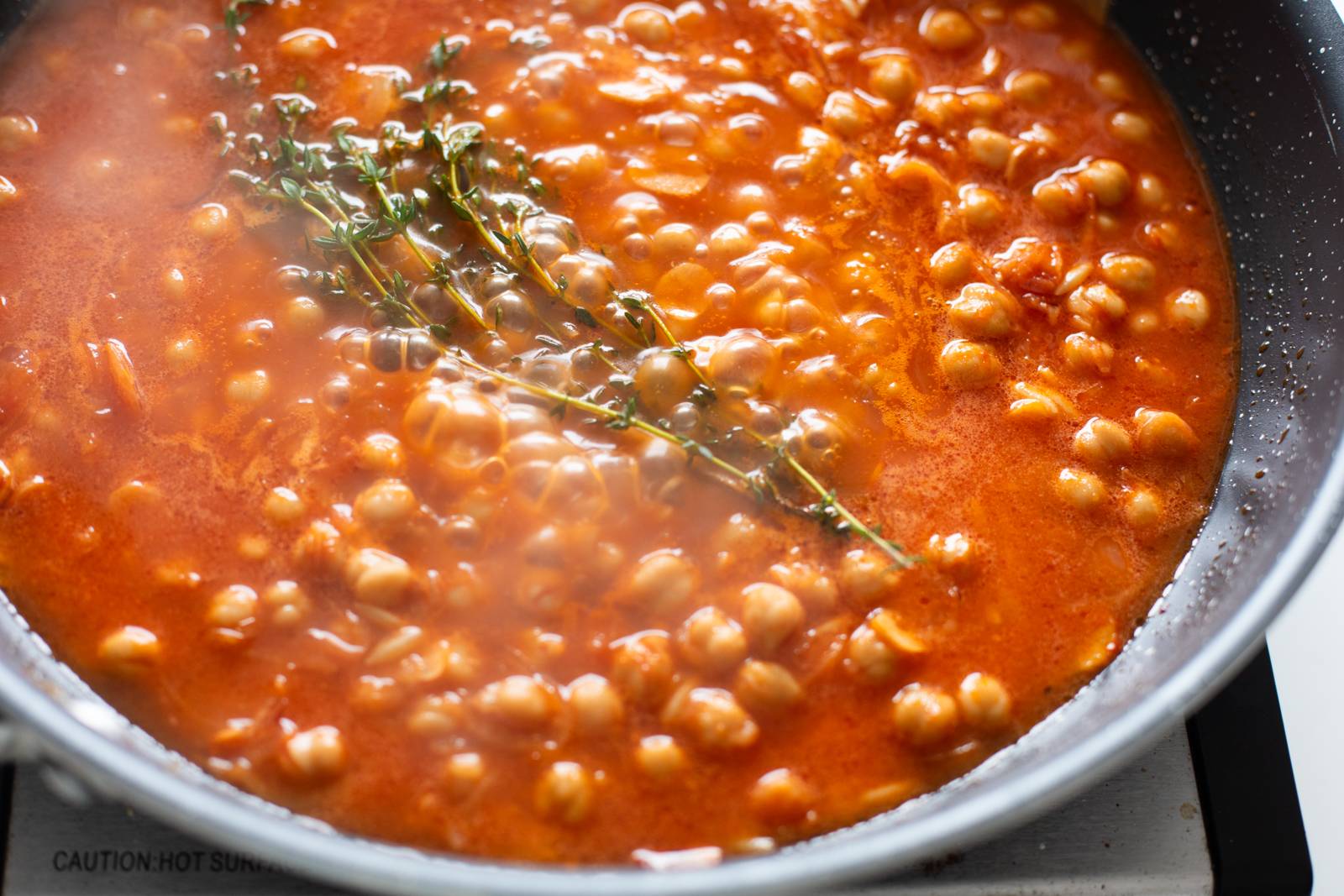 Orzo simmering in a skillet with broth and thyme.