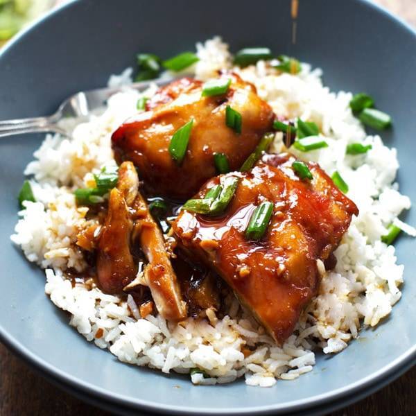Sticky bourbon chicken in a bowl with rice and topped with green onion.