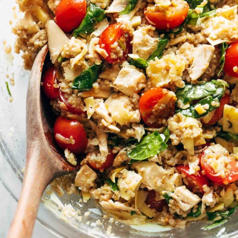 A quinoa chicken salad with tomatoes, and spinach in a glass bowl.