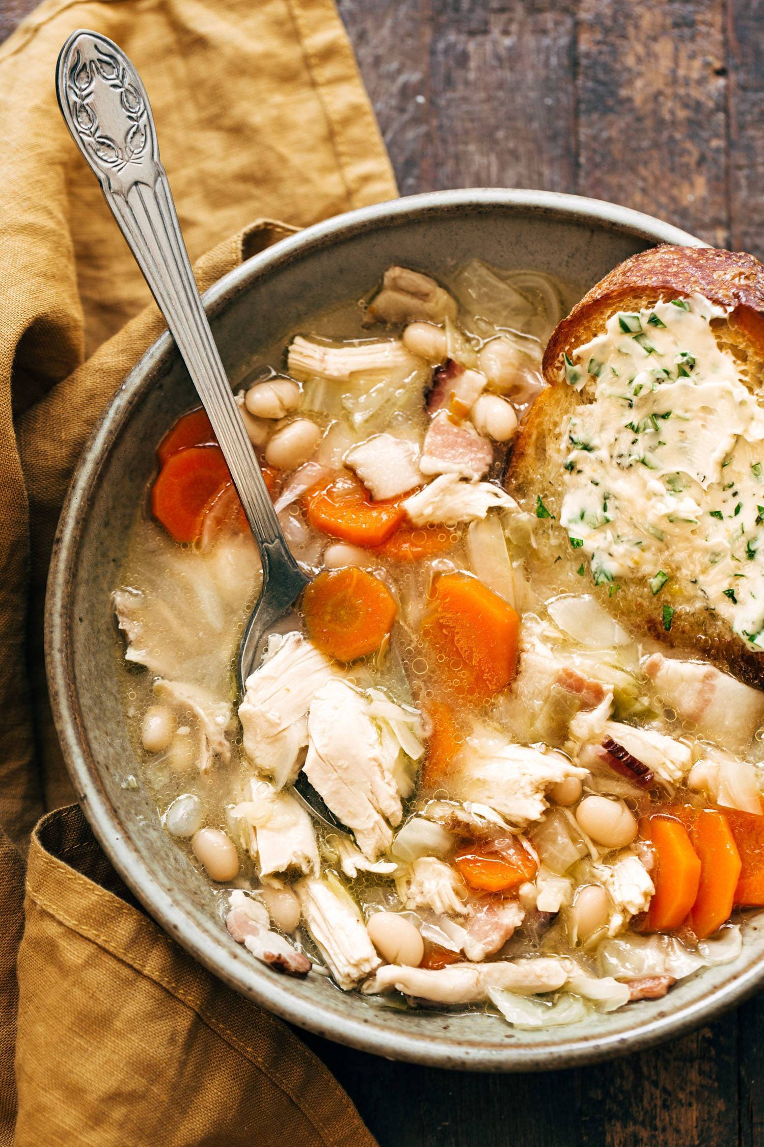 Chicken stew in a bowl with a spoon and garlic herb butter bread.