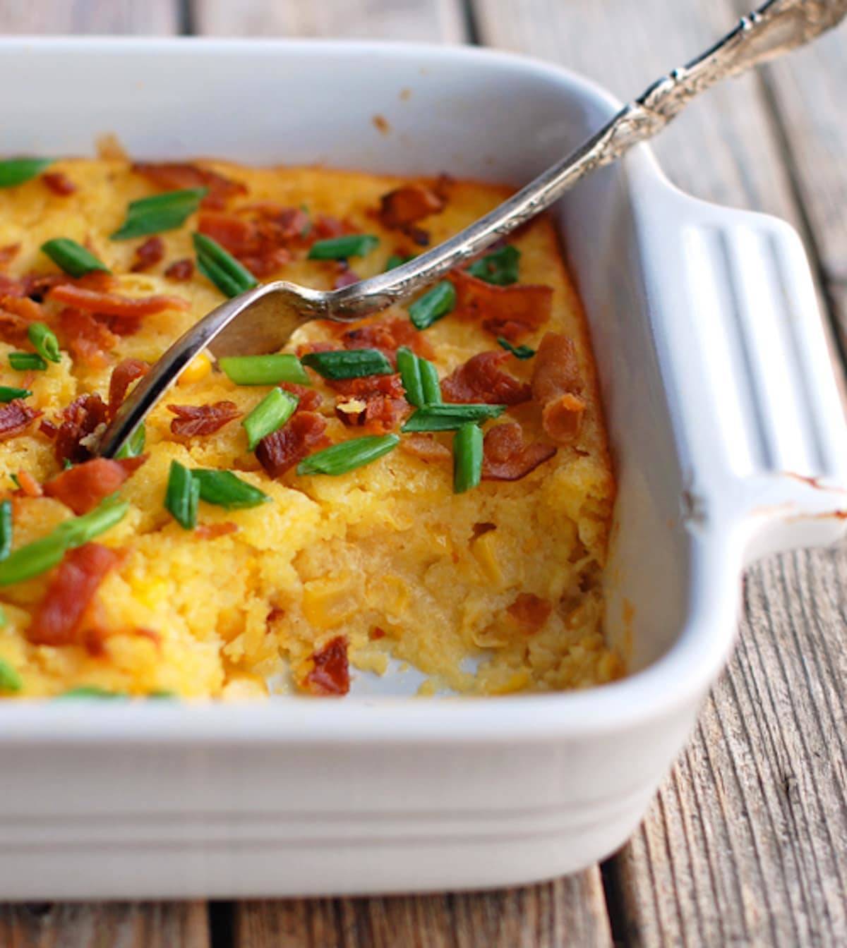 Creamy baked corn with a spoon in a white baking dish.