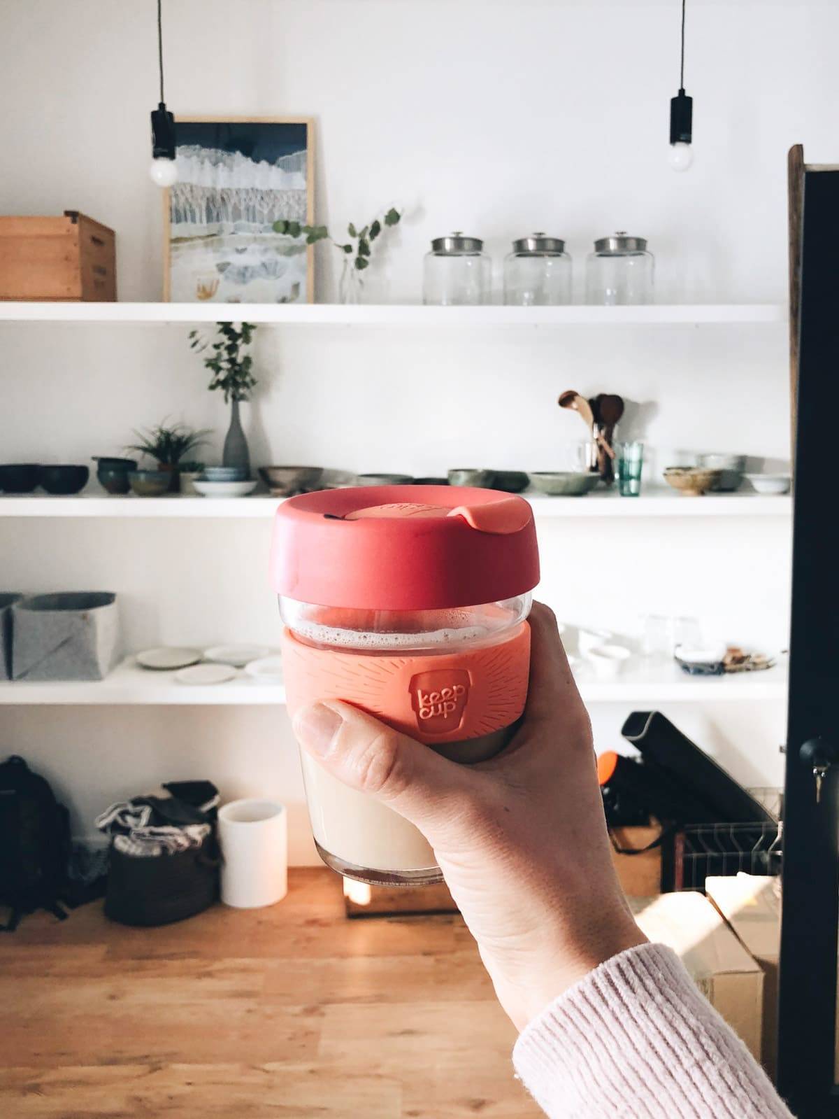 A hand holding a mug in front of shelves.