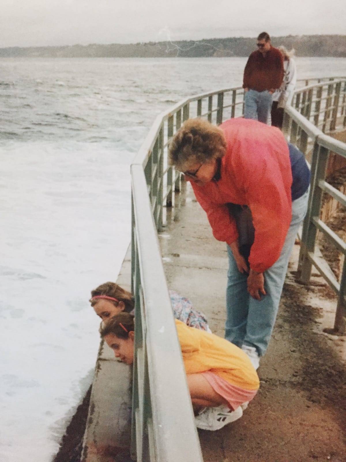 Woman looking at two girls on a deck over water.